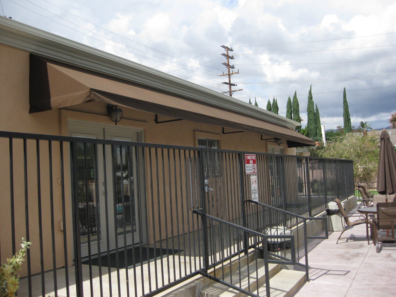 Apartment patio with black metal railing, sliding doors, and outdoor seating under a cloudy sky