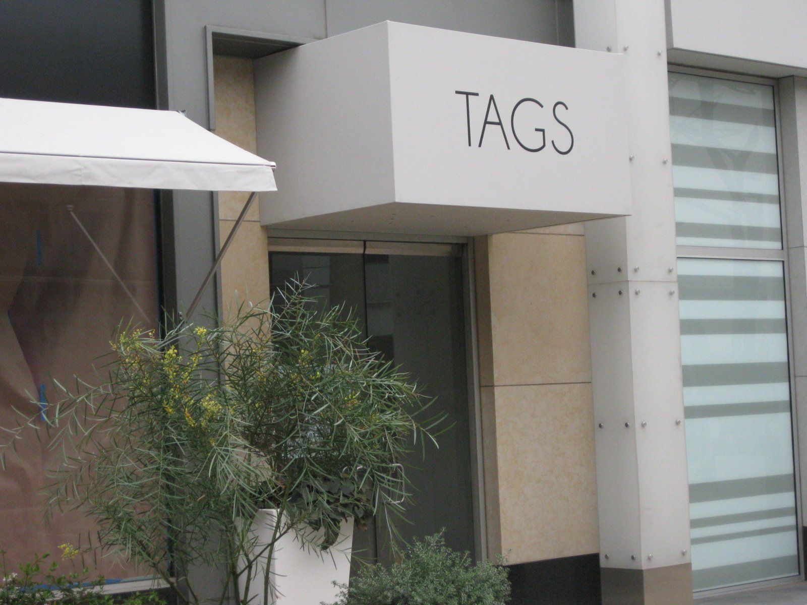 Storefront entrance with a “TAGS” sign and potted greenery beside the door.
