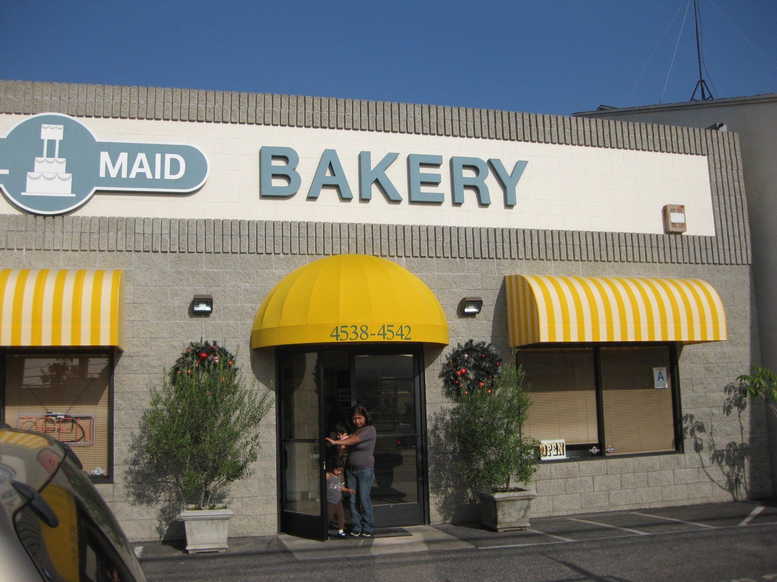 Maid Bakery storefront with yellow awnings and a person standing in the doorway