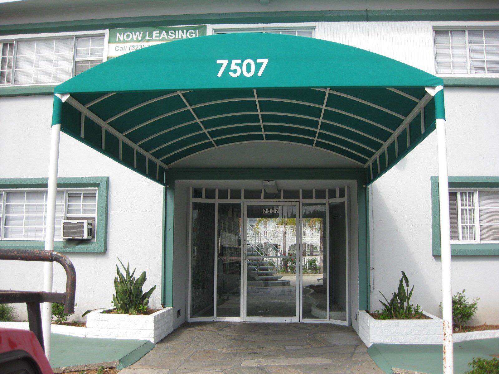 Green awning over glass entrance of a building labeled 7507 with planters on both sides