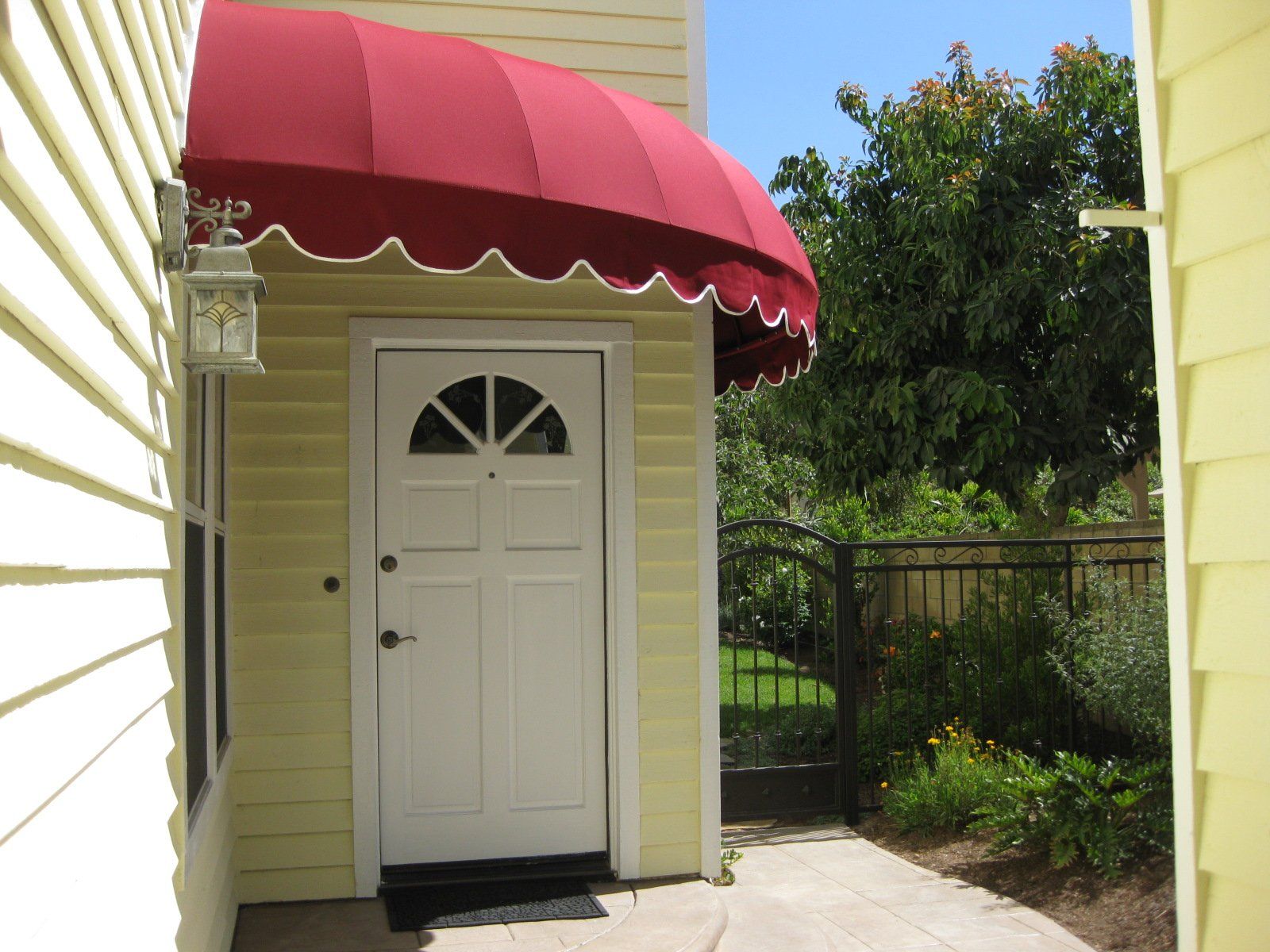 White side door with red awning at a house entrance, beside a fenced garden path.