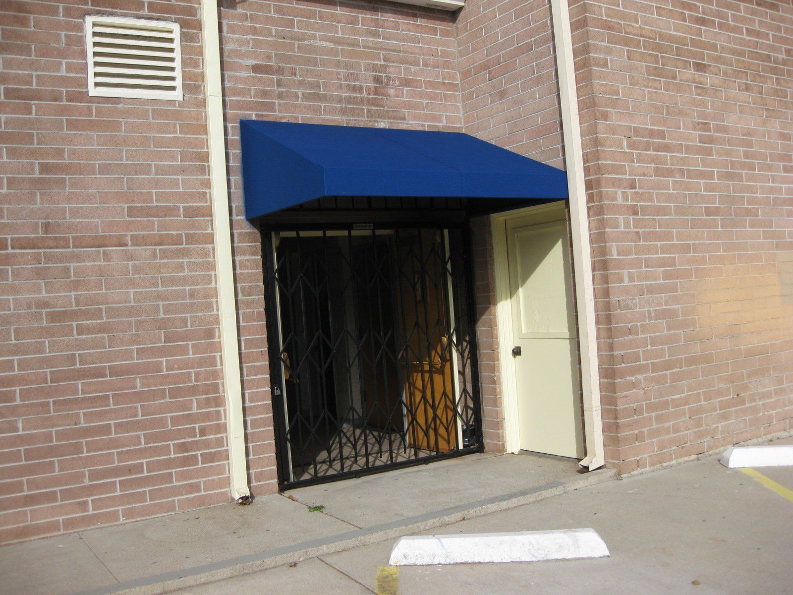 Brick building entrance with blue awning, black metal gate, and white door panel