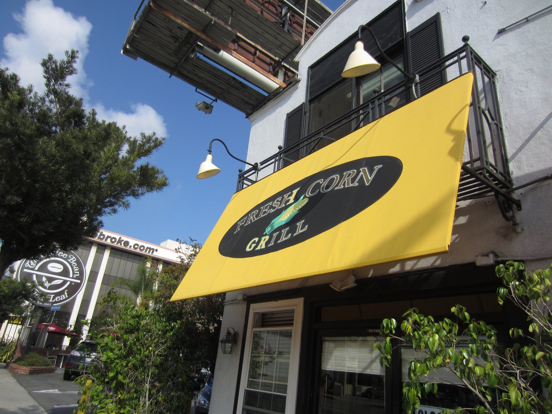 Yellow awning on a storefront with black lettering, viewed from a sidewalk under a blue sky