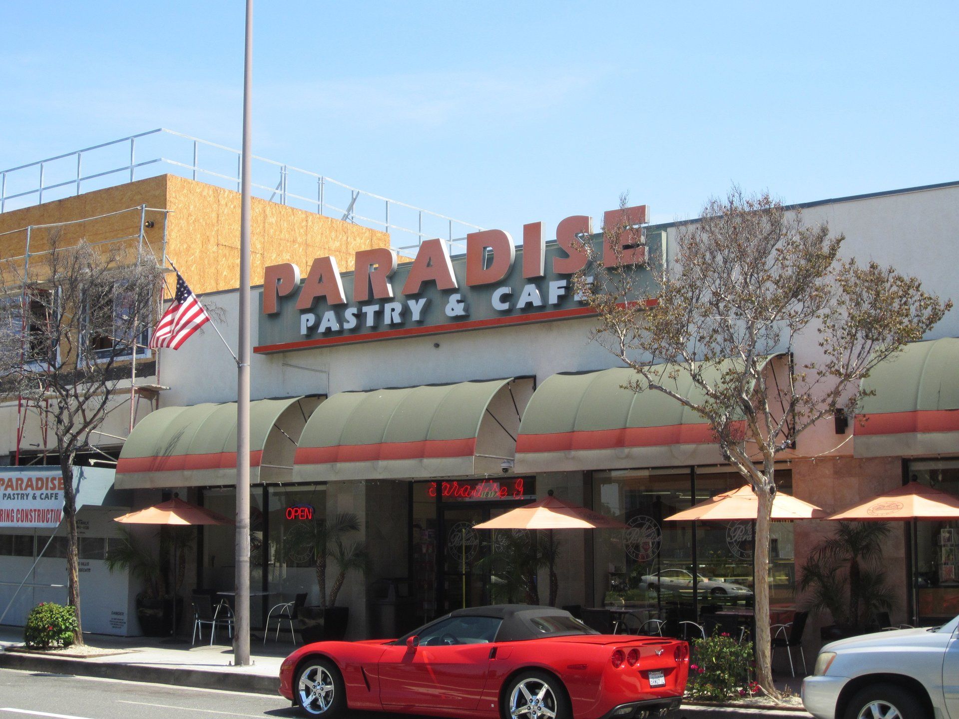 Paradise Pastry & Cafe storefront with red sports car parked outside and American flag on the left