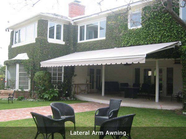 Brick house with ivy, white awning, and patio chairs in a green backyard