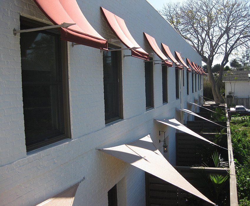 White building exterior with red awnings over windows and small shaded balconies along the side