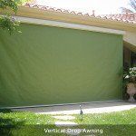 Green vertical drop awning covering a patio, with a tiled roof above.