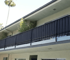 Apartment building balcony with black railings and white exterior walls, seen from below