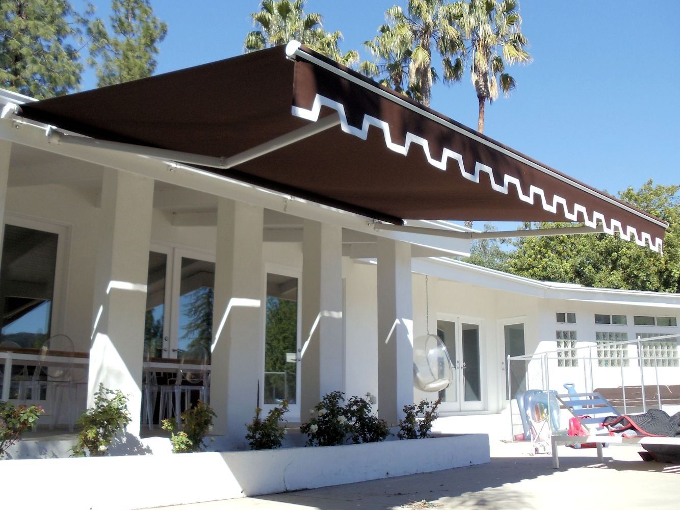 White building with dark roof, columns, and small potted plants in front, viewed in bright daylight