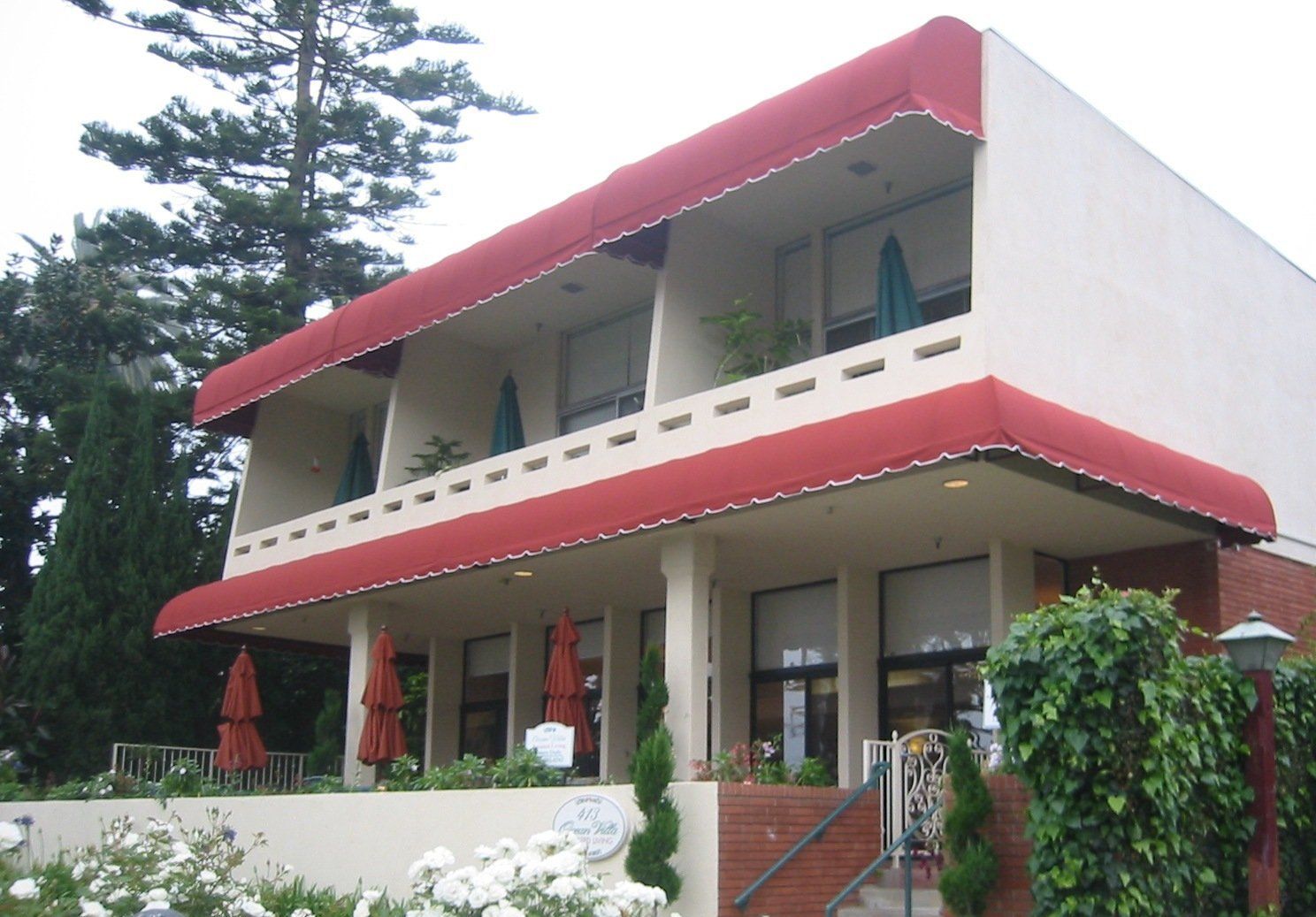 Modern white two-story house with red awnings, balconies, and a garden in front