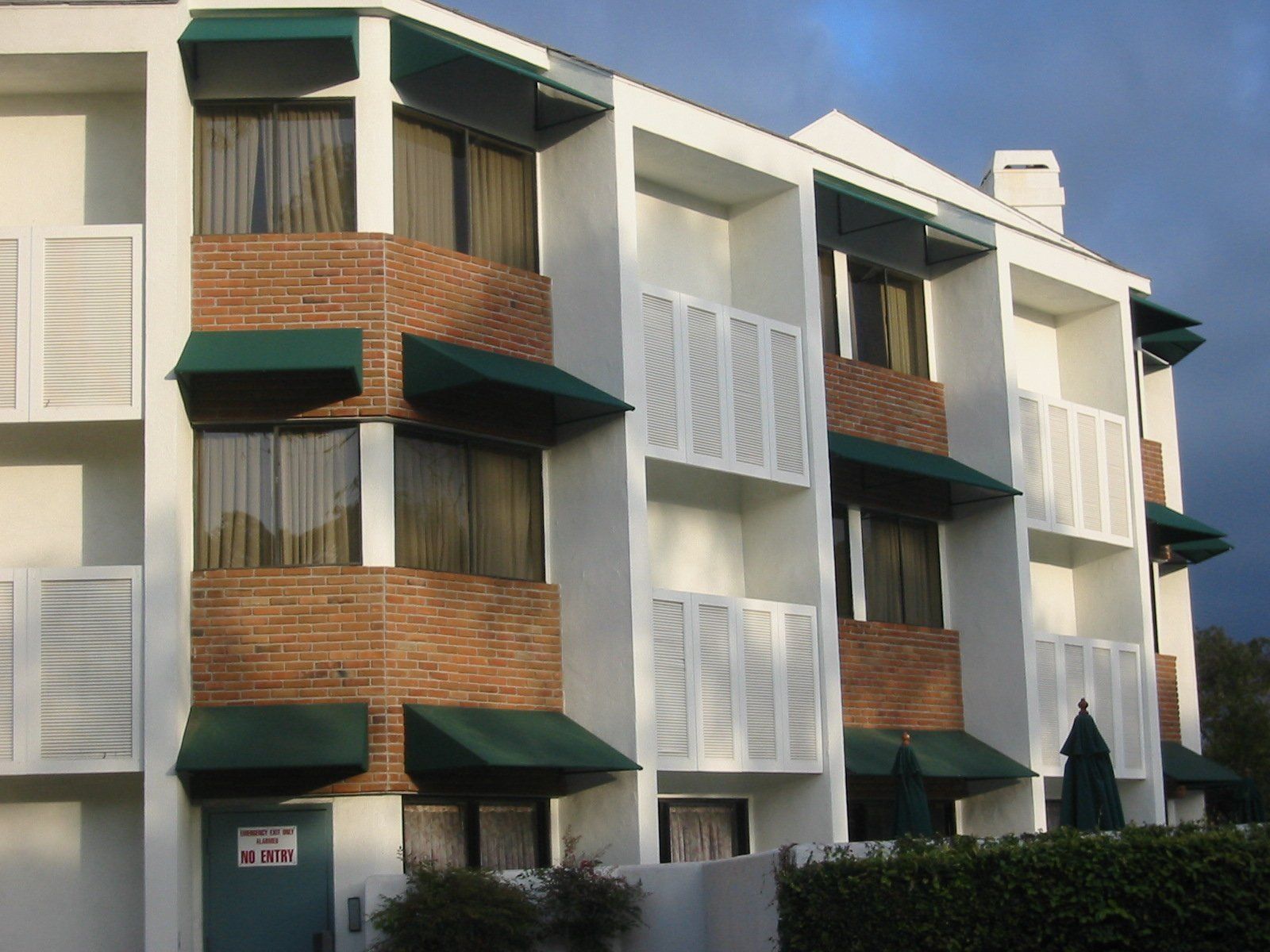 Modern apartment building with white walls, brick balconies, and green awnings under a blue sky