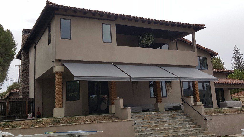 Two-story beige house with awnings, stone steps, and a covered front porch