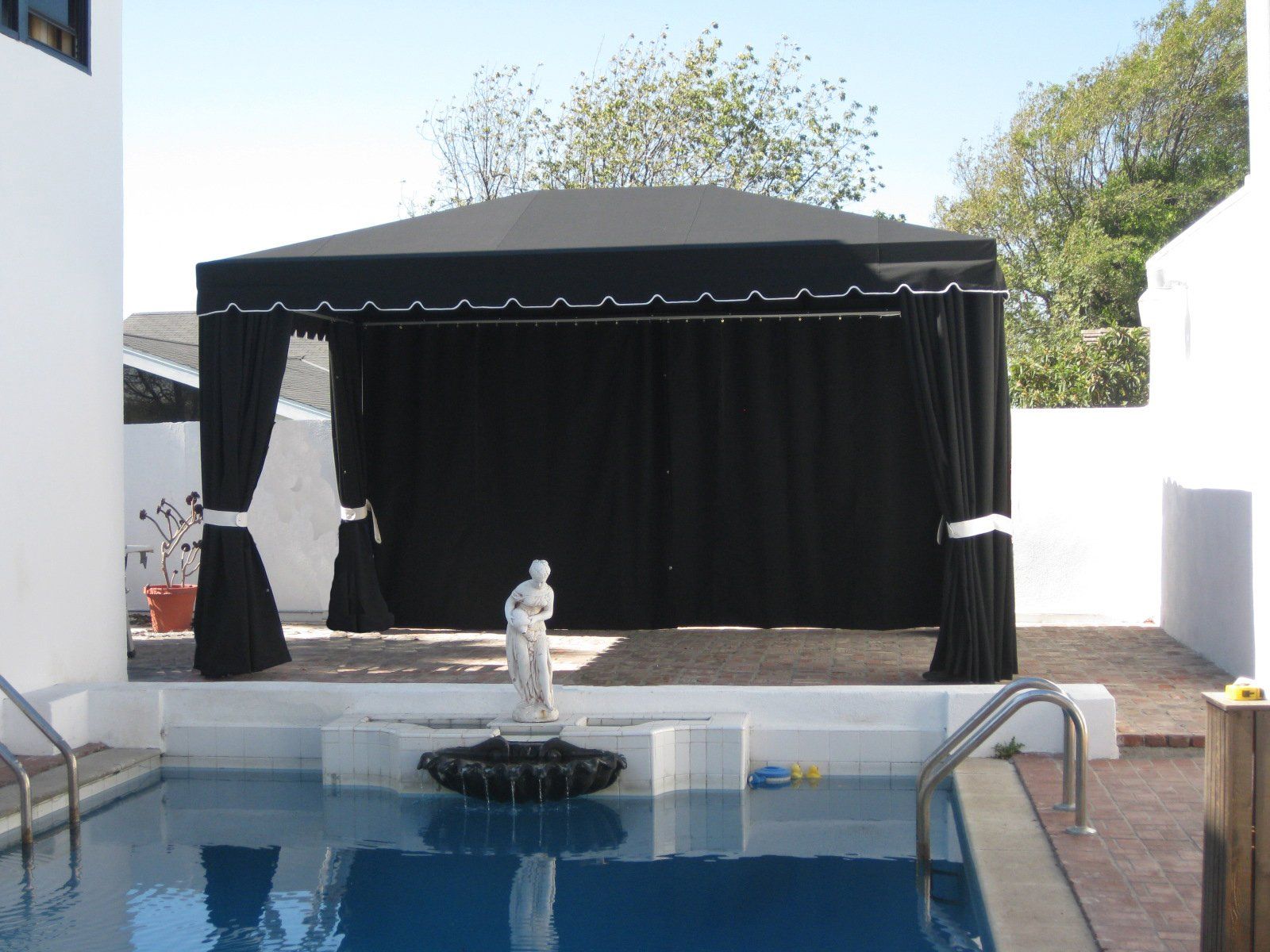 Backyard pool with white statue fountain and black canopy stage beside the water