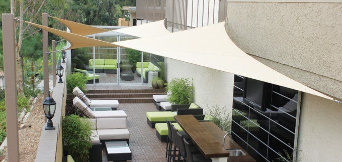 Covered outdoor patio with lounge seating, tables, and white shade sails in a modern courtyard