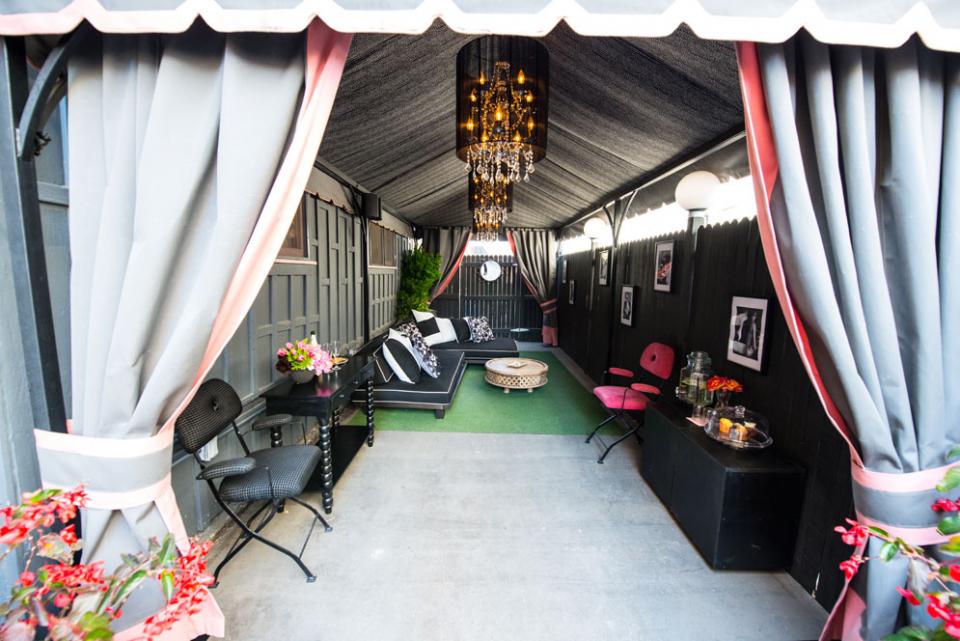Covered outdoor patio with gray curtains, black seating, green carpet, and hanging chandelier in the center