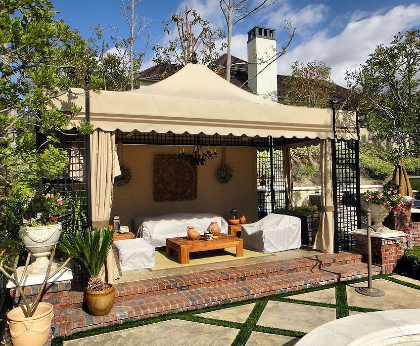 Canopy-covered outdoor lounge with sofa, rug, potted plants, and garden courtyard setting