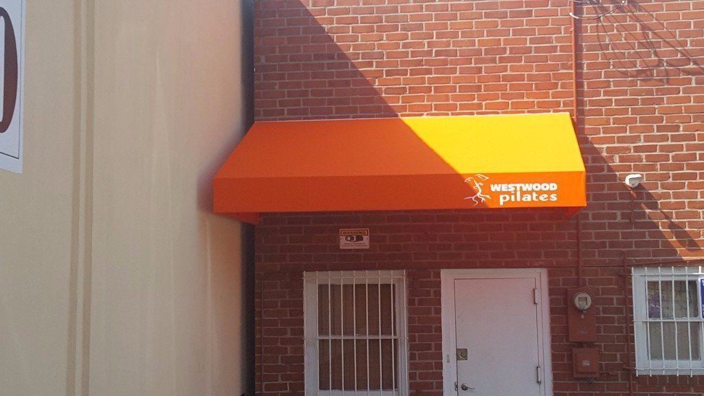 Brick building entrance with an orange and yellow awning over a white door and barred window.