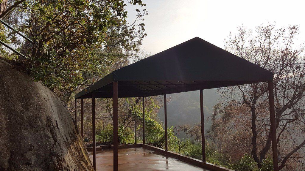 Open-air pavilion on a forested hillside with trees and a rocky overlook