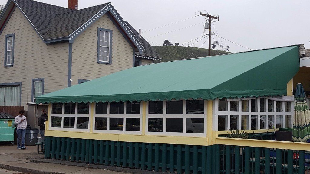 Long green canopy over a cream building beside a sidewalk and house on a street corner