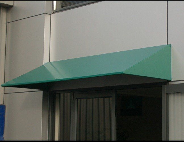 Teal awning over a building entrance with glass doors and gray walls