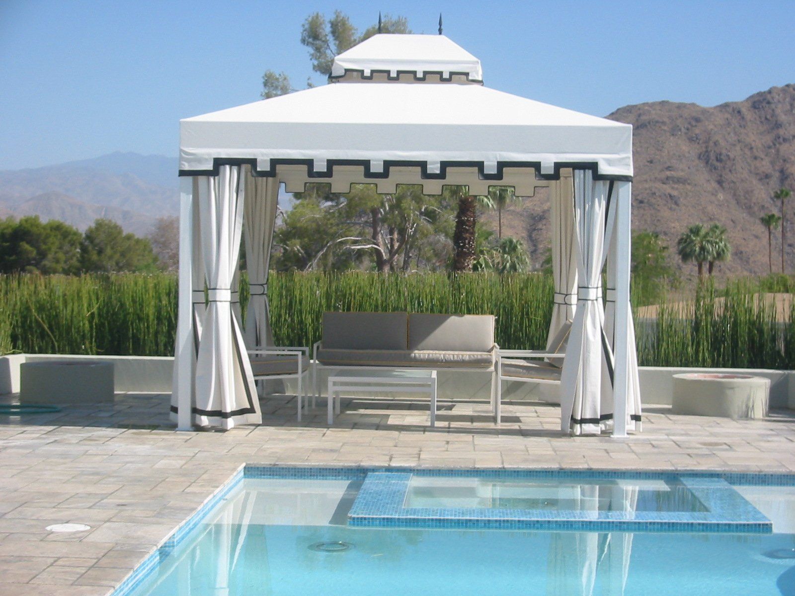 White gazebo by a pool with sheer curtains, patio seating, and mountain views in the background