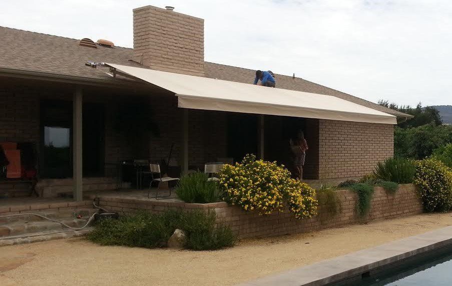 Brick house with covered patio, shrubs, and a swimming pool in front