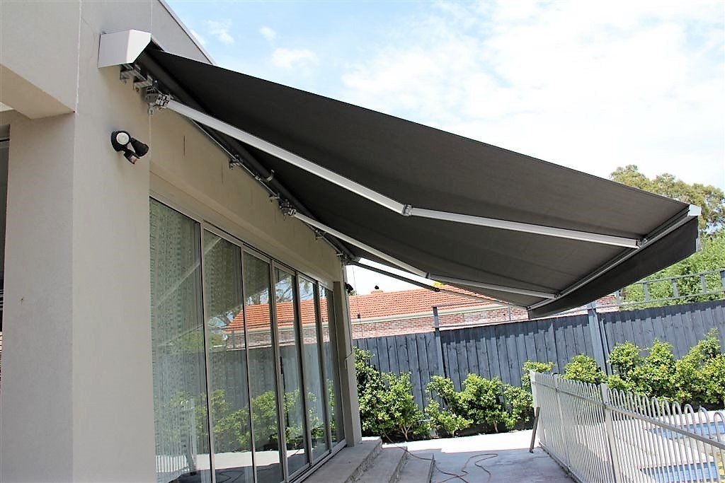 Black retractable awning over a patio beside a house, shading outdoor seating and a fence-lined yard