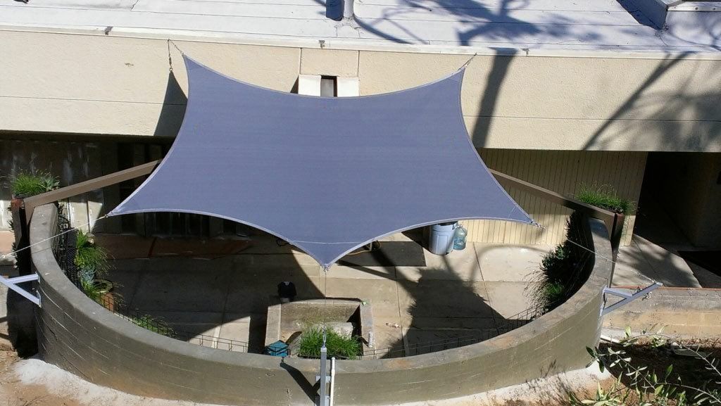 Gray shade sail stretched over a circular fountain in an outdoor courtyard.