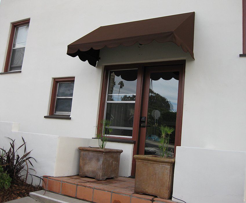 Small entryway with brown awning, glass door, and two planters on a tiled stoop