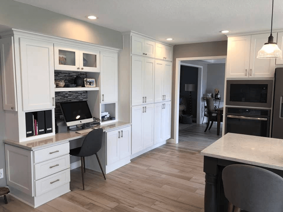 White kitchen with built-in desk, cabinets, and island with gray countertop and appliances.