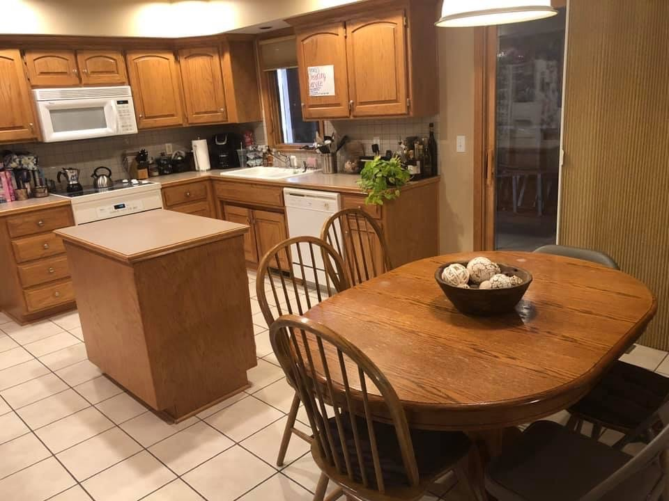 Kitchen with wooden cabinets, appliances, dining table with chairs, and tiled floor.