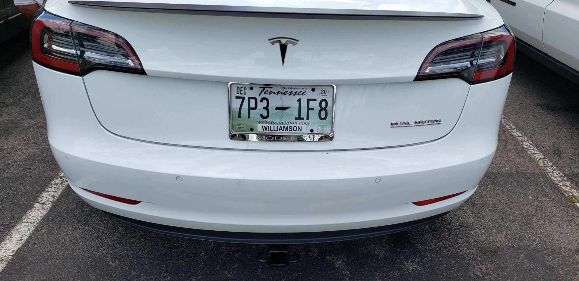 The rear view of a white Tesla sedan parked in a lot, displaying a Tennessee license plate reading 7P3-1F8.