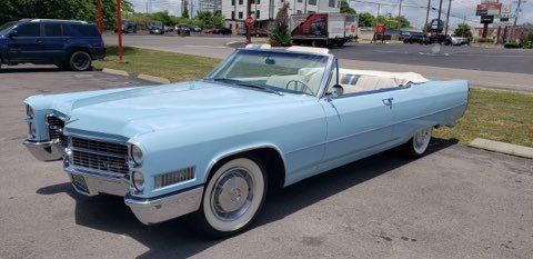 A light blue vintage Cadillac convertible parked on an asphalt lot on a sunny day.