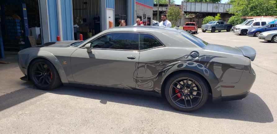 A grey Dodge Challenger with widebody fenders and a dark decorative graphic on the rear quarter panel parked outside.