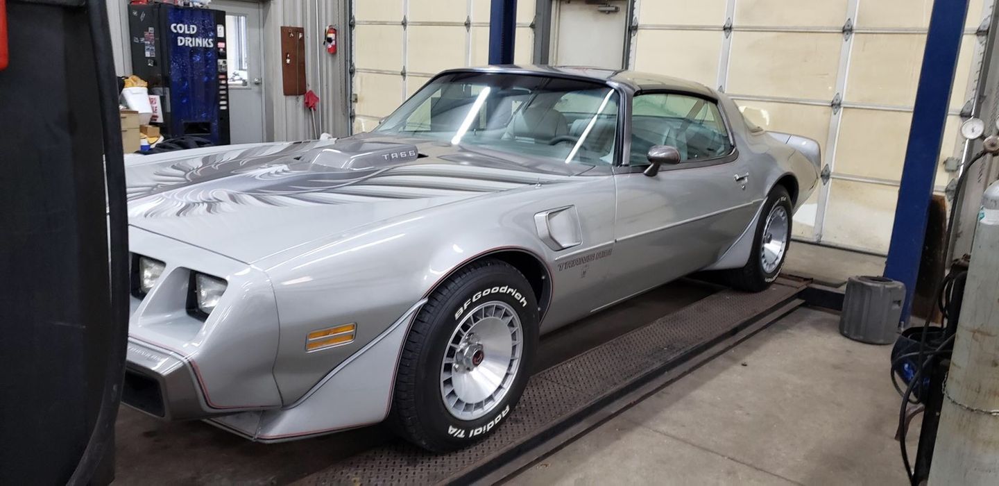 A silver Pontiac Firebird Trans Am parked inside a garage workshop on an auto lift.