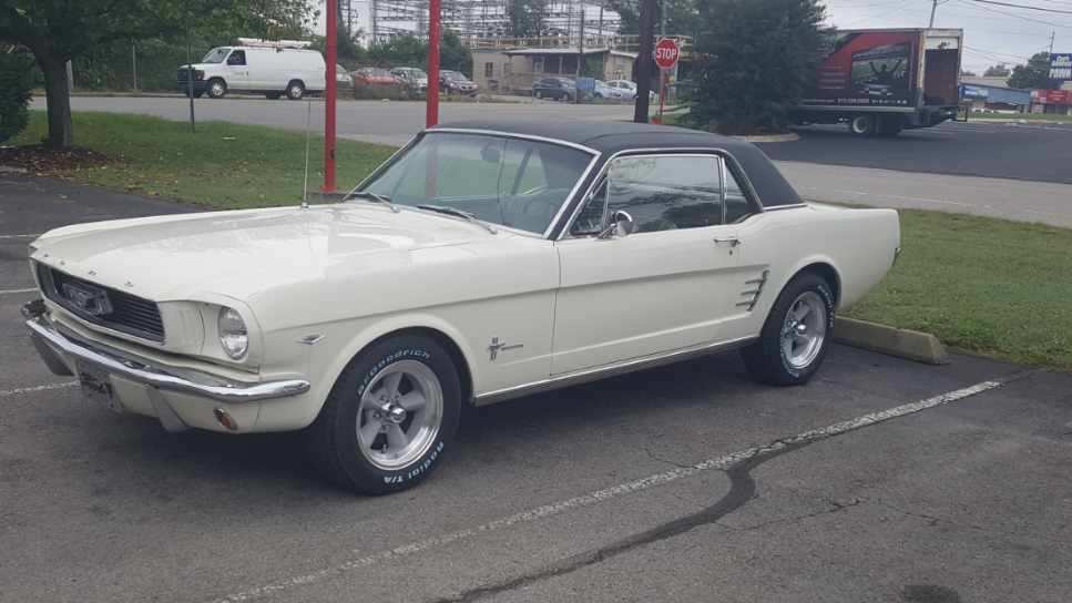A white classic Ford Mustang convertible with a black top parked in an asphalt lot.