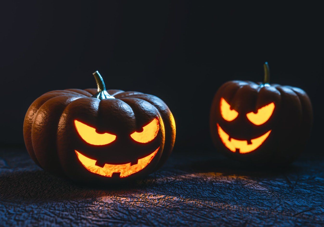 Two lit jack-o'-lanterns with glowing eyes and toothy grins on a dark surface.
