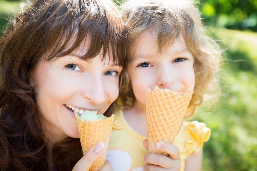 Woman and child smiling and eating ice cream cones outdoors.
