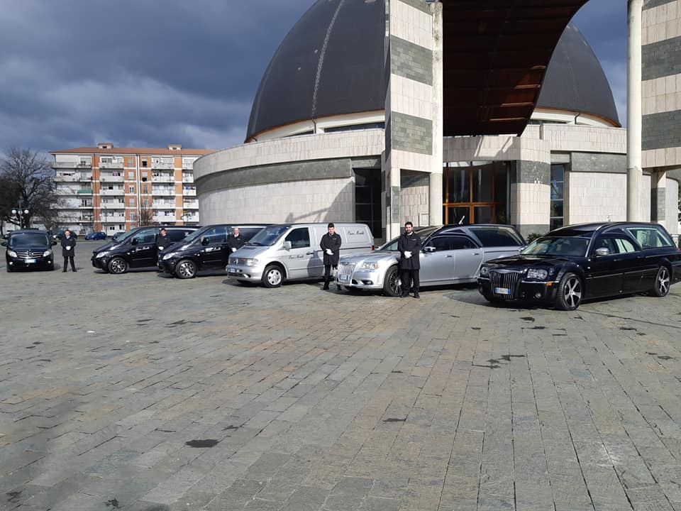 Auto parcheggiate in fila davanti a un grande edificio moderno con cupole curve e una piazza pavimentata