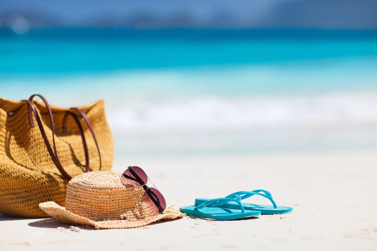 Handtasche, Sommerhut und Flip Flops am Strand
