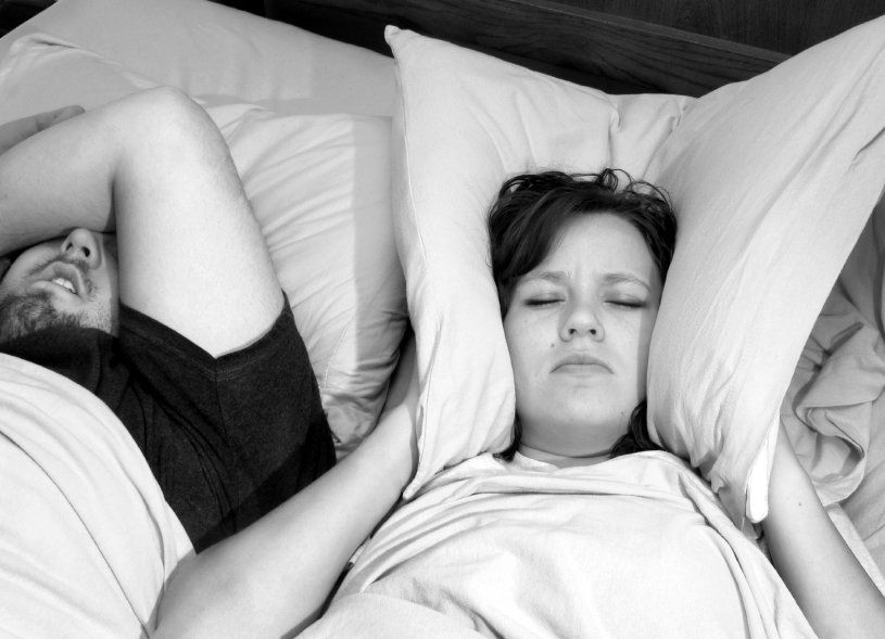 Woman holding both ends of a pillow to her ears attempting to block sound of her partner snoring.