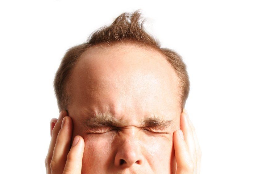 Close up of man wincing in pain and holding both hands to his jaw from TMJ.