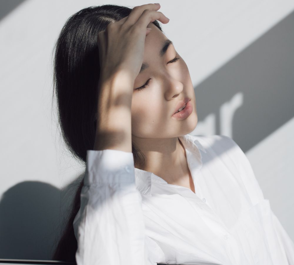 Young woman in white blouse hides her eyes in the shade while suffering a headache.