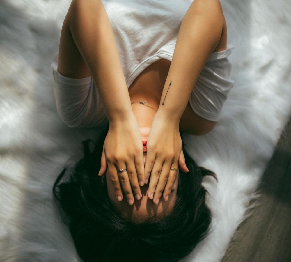 Woman laying upside down and covering her face with both hands from TMJ pain while sleeping.