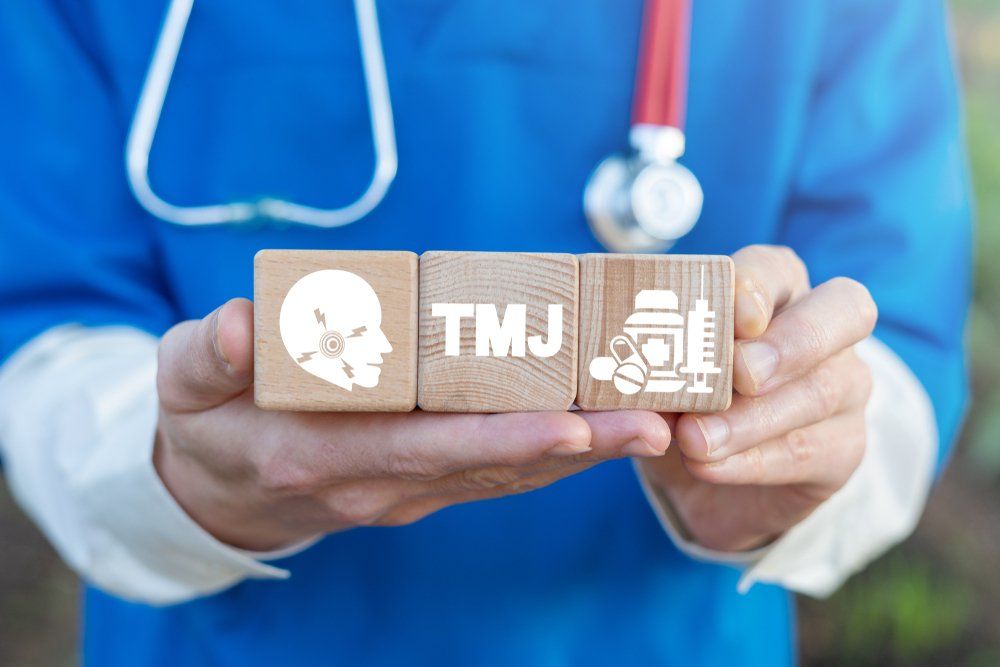 Close view of doctor in blue scrubs with stethoscope holding three wooden blocks with white symbols for TMJ treatment.