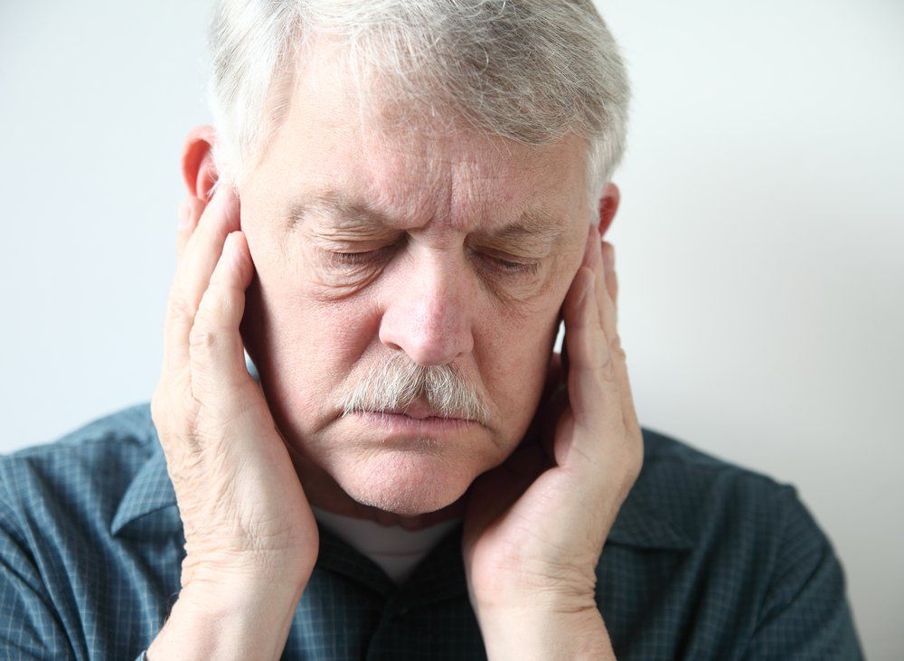 Older man holds ends of his jaw while looking down and experiencing a TMJ flare up.