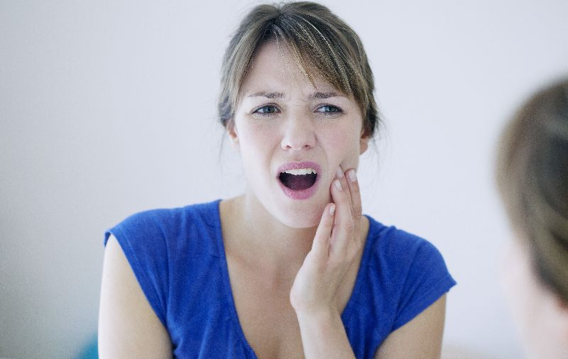 Woman in blue blouse holds her jaw with her mouth open.
