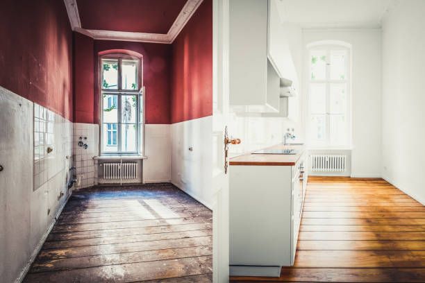 Room renovation, split view: red-painted room before, white-painted kitchen after, wood floors, sunlight through windows.