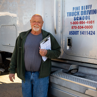 man with jeans and jacket standing in front of semi with clipboard