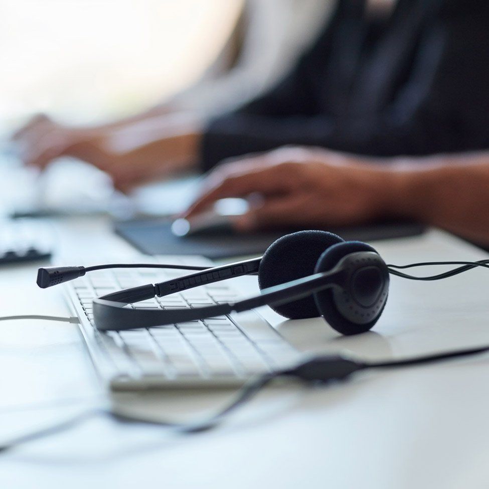 Headset on keyboard in front of person using a computer.